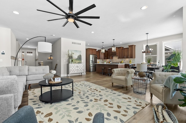 living area with ceiling fan with notable chandelier, visible vents, dark wood-style flooring, and recessed lighting