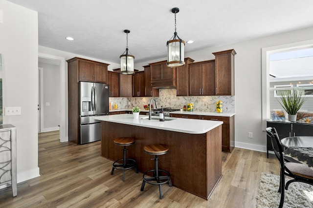 kitchen featuring decorative backsplash, hanging light fixtures, light countertops, stainless steel refrigerator with ice dispenser, and a sink