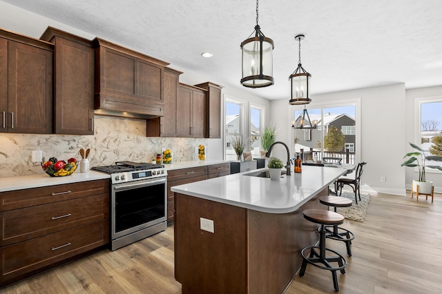 kitchen featuring gas stove, light countertops, a sink, and an island with sink