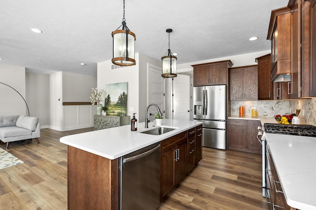 kitchen featuring stainless steel appliances, decorative light fixtures, a sink, and a center island with sink