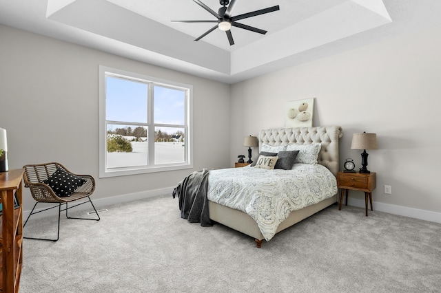 carpeted bedroom with ceiling fan, a raised ceiling, and baseboards