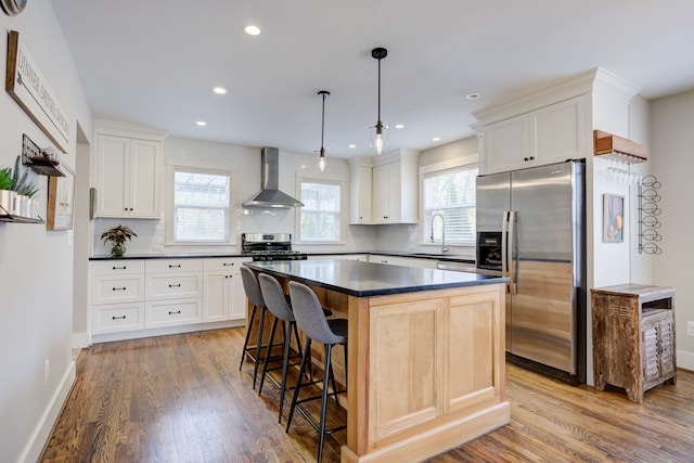 kitchen featuring hanging light fixtures, appliances with stainless steel finishes, plenty of natural light, and wall chimney range hood