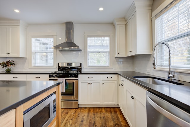 kitchen with dark wood-type flooring, wall chimney range hood, sink, decorative backsplash, and appliances with stainless steel finishes