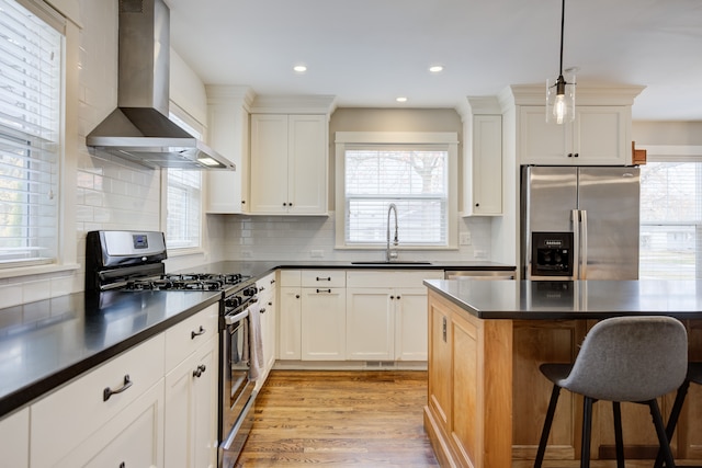 kitchen featuring sink, wall chimney exhaust hood, stainless steel appliances, light hardwood / wood-style flooring, and pendant lighting