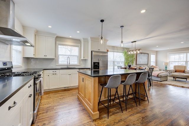 kitchen featuring appliances with stainless steel finishes, wall chimney exhaust hood, white cabinets, hardwood / wood-style floors, and a kitchen island