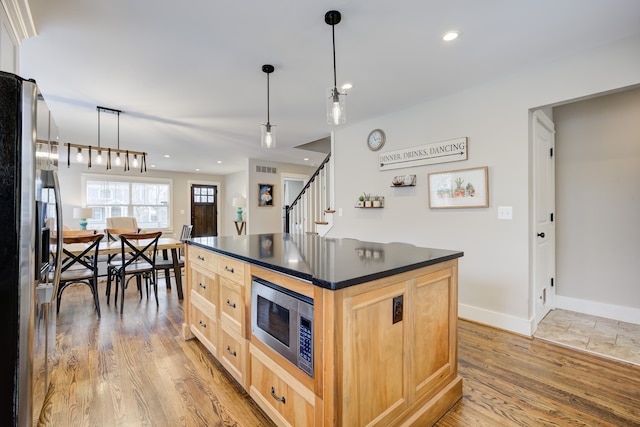 kitchen with a center island, light brown cabinets, appliances with stainless steel finishes, decorative light fixtures, and light hardwood / wood-style floors