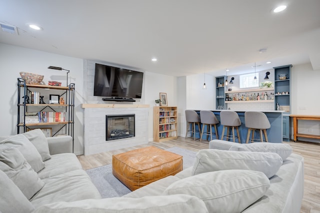 living room with bar area, light wood-type flooring, and a large fireplace