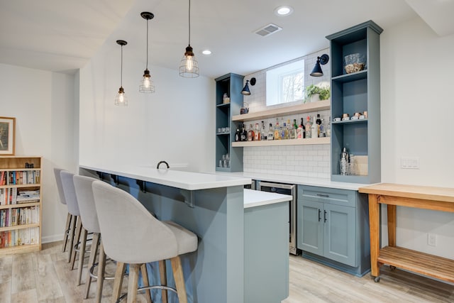 bar featuring pendant lighting, light hardwood / wood-style floors, blue cabinetry, and backsplash