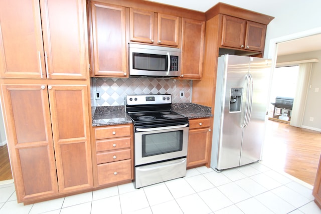 kitchen with light wood-type flooring, backsplash, appliances with stainless steel finishes, and dark stone counters