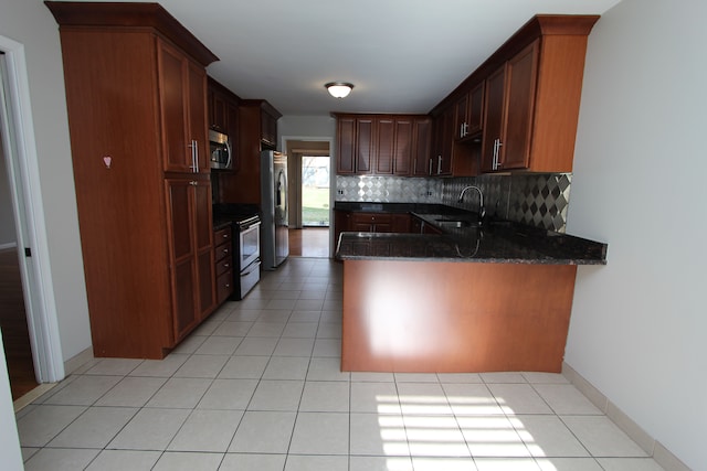 kitchen featuring sink, kitchen peninsula, dark stone counters, decorative backsplash, and appliances with stainless steel finishes