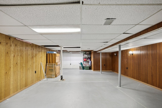 basement featuring a paneled ceiling and wood walls