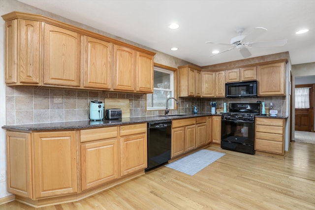 kitchen with dark stone countertops, sink, black appliances, and light hardwood / wood-style flooring