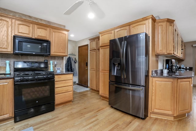 kitchen featuring dark stone counters, black appliances, light wood finished floors, and decorative backsplash