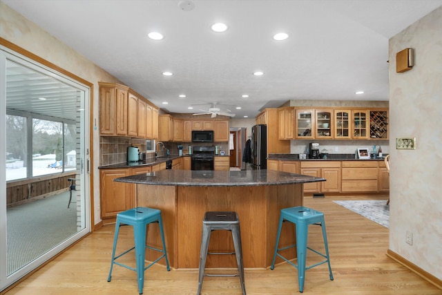 kitchen with black appliances, a kitchen island, glass insert cabinets, and a kitchen breakfast bar