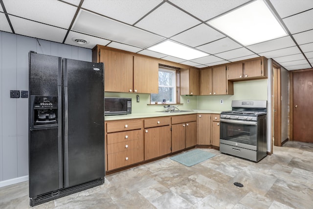 kitchen with brown cabinetry, a drop ceiling, light countertops, black appliances, and a sink