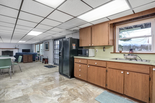 kitchen with brown cabinets, light countertops, open floor plan, a sink, and black appliances