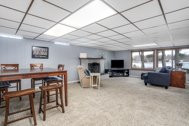 carpeted living room with a drop ceiling and a brick fireplace