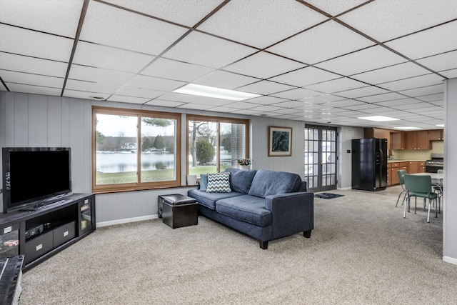 living area with baseboards, a drop ceiling, and light colored carpet