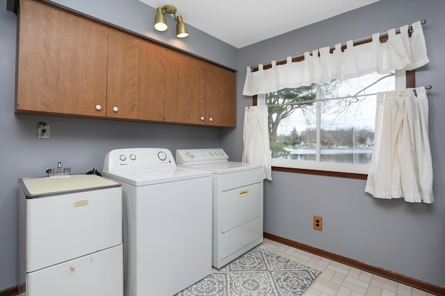 clothes washing area with light floors, cabinet space, a water view, washer and dryer, and baseboards