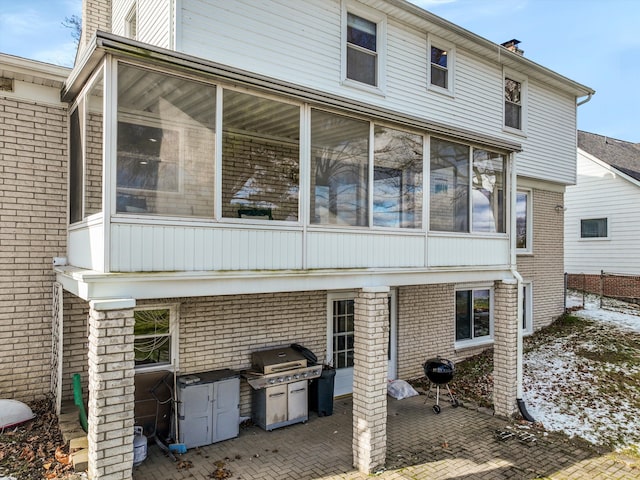 back of property with a patio, brick siding, a chimney, and a sunroom