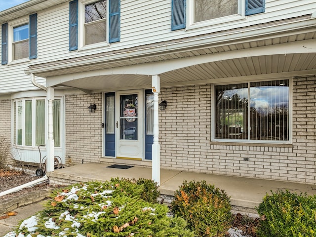 entrance to property with a porch and brick siding