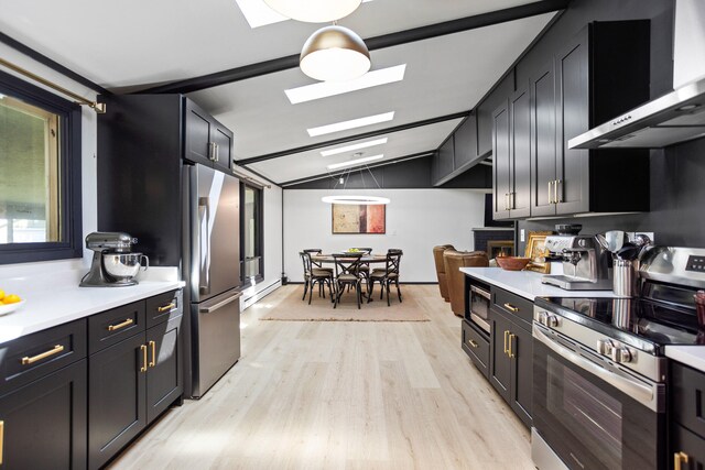 kitchen featuring wall chimney range hood, light hardwood / wood-style flooring, a baseboard heating unit, lofted ceiling with skylight, and appliances with stainless steel finishes