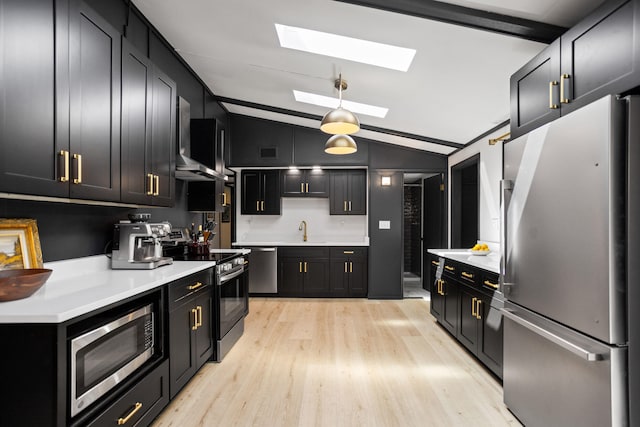 kitchen featuring sink, pendant lighting, vaulted ceiling with skylight, appliances with stainless steel finishes, and light wood-type flooring