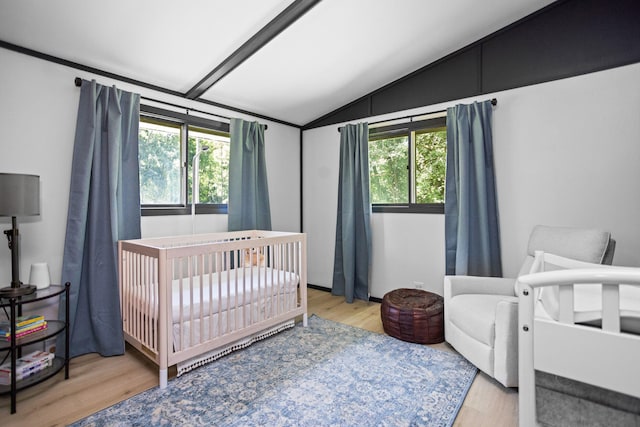 bedroom with a crib, light wood-type flooring, vaulted ceiling, and multiple windows