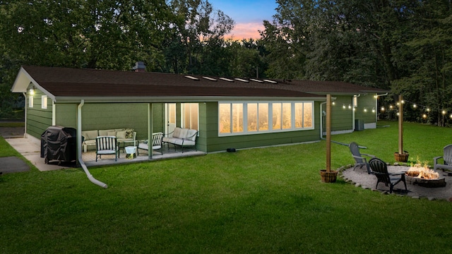 back house at dusk featuring a lawn, a patio area, and an outdoor living space with a fire pit