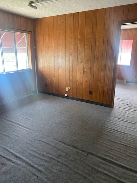 spare room with a textured ceiling, dark carpet, and wooden walls