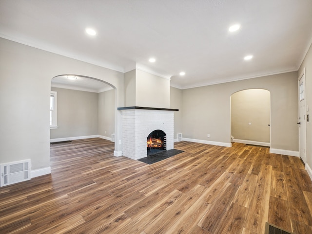 unfurnished living room featuring a brick fireplace, ornamental molding, and hardwood / wood-style flooring