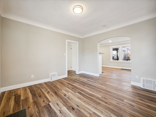 empty room featuring wood-type flooring, a textured ceiling, and crown molding