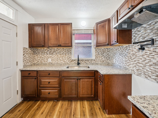 kitchen with hardwood / wood-style floors, sink, decorative backsplash, a textured ceiling, and light stone counters