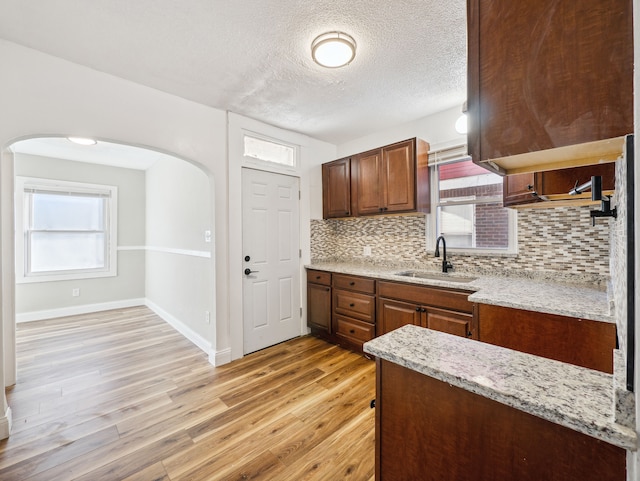 16162 Normandy St, Detroit, MI 48221 - kitchen featuring a sink, decorative backsplash, arched walkways, light wood finished floors, and light stone counters