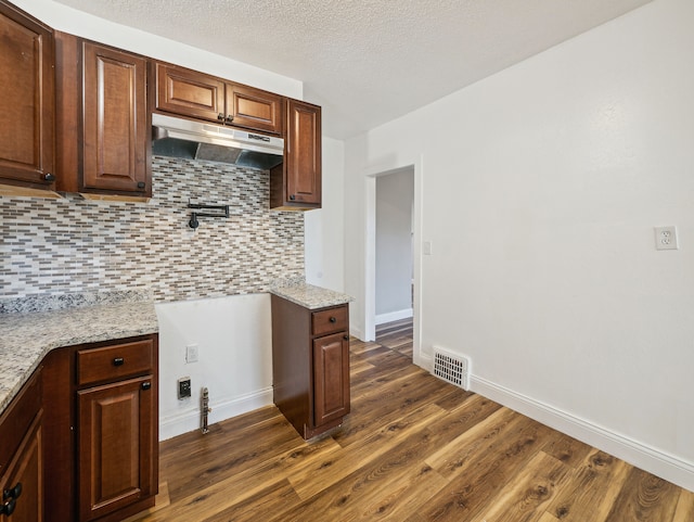 kitchen featuring decorative backsplash, light stone counters, dark wood-type flooring, and a textured ceiling