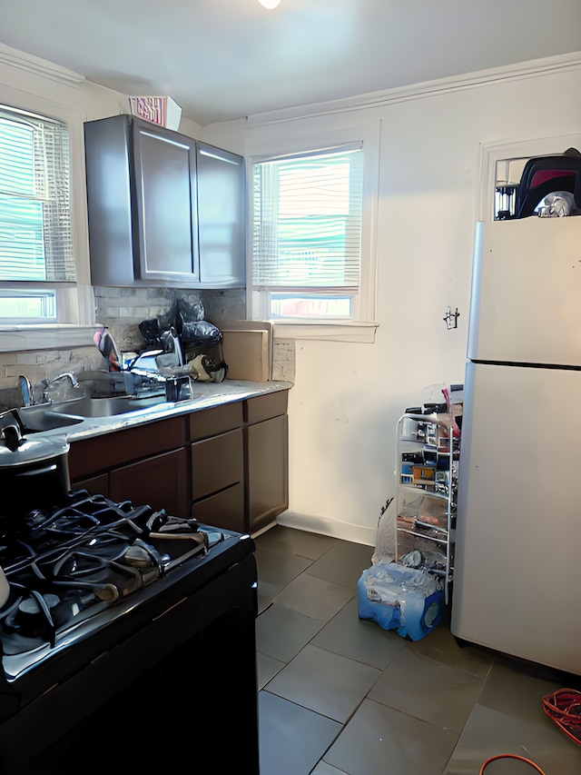 kitchen with black range with gas stovetop, white refrigerator, tasteful backsplash, and a healthy amount of sunlight