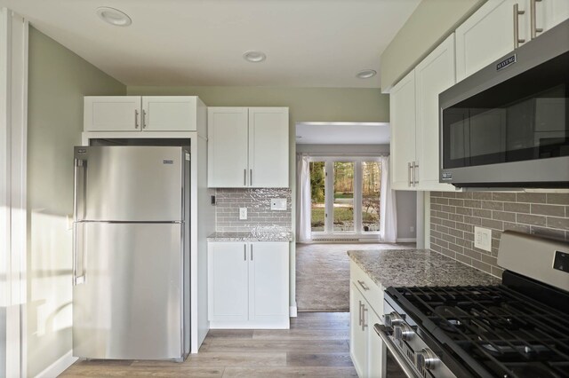 kitchen featuring white cabinetry, light stone countertops, stainless steel appliances, tasteful backsplash, and light wood-type flooring