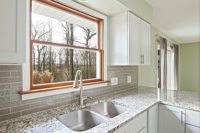 kitchen featuring decorative backsplash, white cabinetry, light stone countertops, and sink