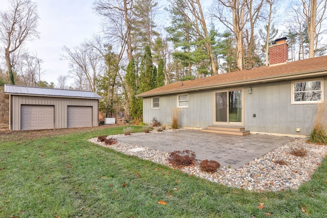 back of house with a lawn, a patio area, a garage, and an outbuilding