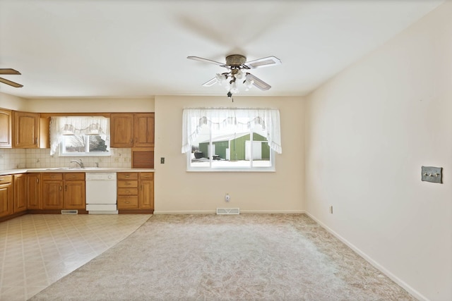 kitchen featuring sink, ceiling fan, white dishwasher, tasteful backsplash, and light colored carpet