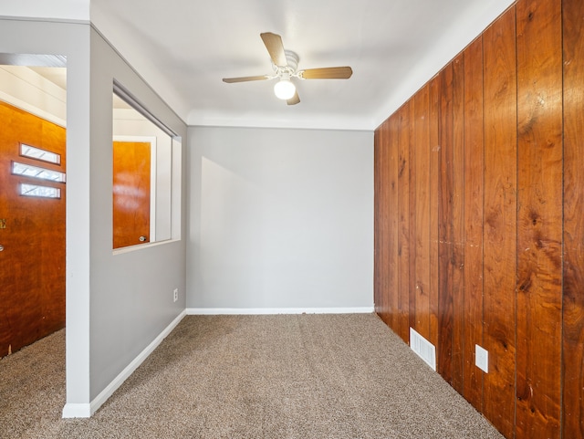 unfurnished room with carpet, ceiling fan, and wooden walls