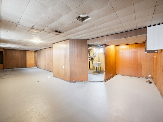 basement featuring a paneled ceiling, wood walls, and sink