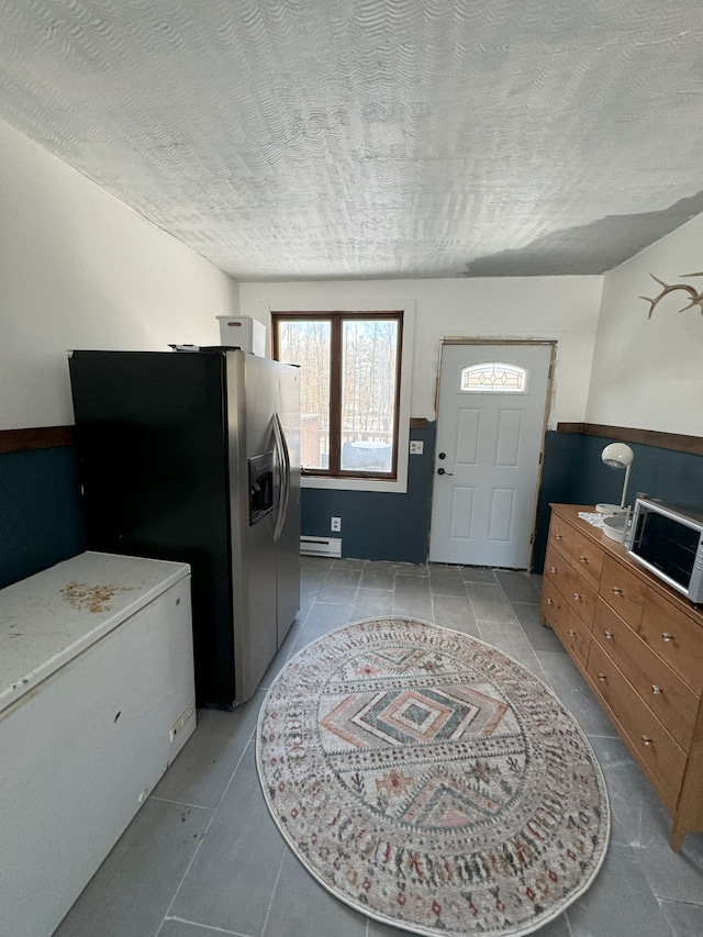 laundry area featuring baseboard heating, light tile patterned floors, and a textured ceiling