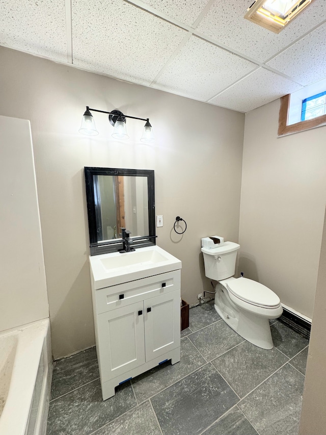 bathroom featuring a paneled ceiling, a washtub, vanity, and toilet