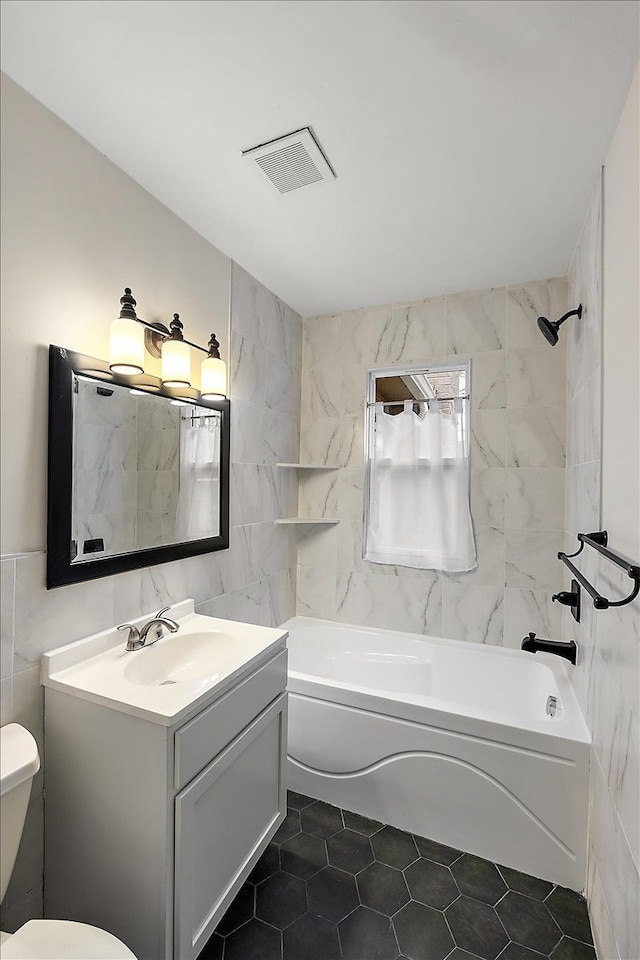 full bathroom with tiled shower / bath combo, tile patterned flooring, toilet, vanity, and tile walls