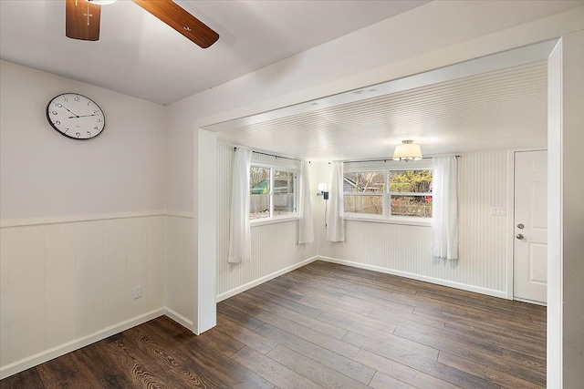 spare room featuring ceiling fan, dark wood-type flooring, and wood walls