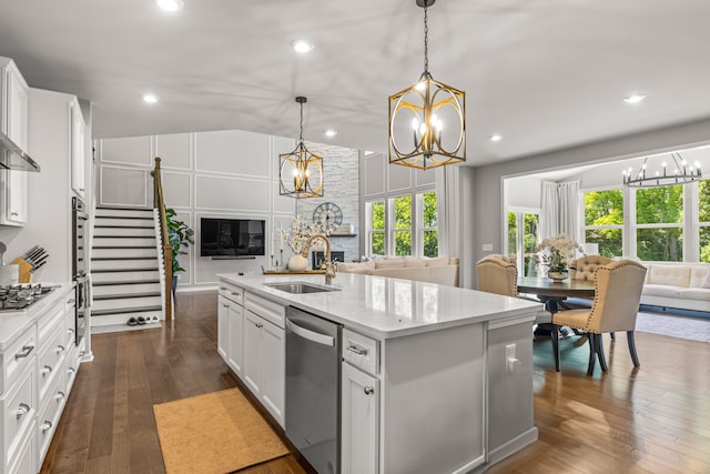 kitchen with white cabinetry, sink, stainless steel appliances, decorative light fixtures, and a kitchen island with sink