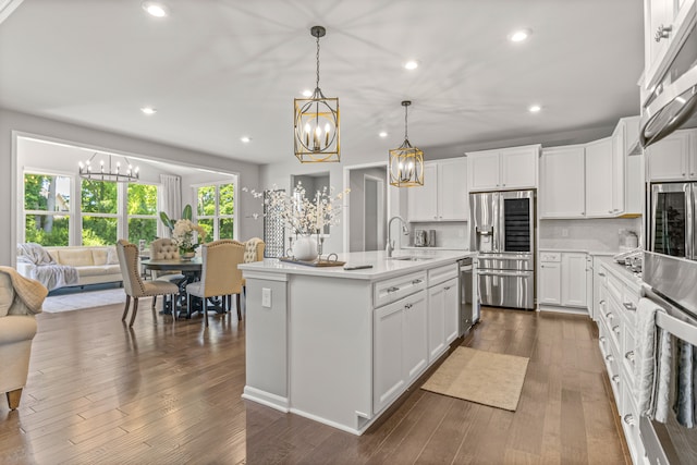 kitchen featuring stainless steel appliances, a kitchen island with sink, sink, white cabinets, and hanging light fixtures