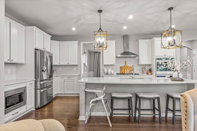 kitchen with decorative light fixtures, stainless steel appliances, white cabinetry, and wall chimney range hood