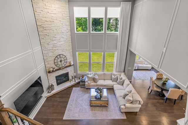 living room featuring a healthy amount of sunlight, a stone fireplace, and dark wood-type flooring